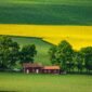 Captivating view of a red farmhouse amidst green and yellow fields in Gränna, Sweden.